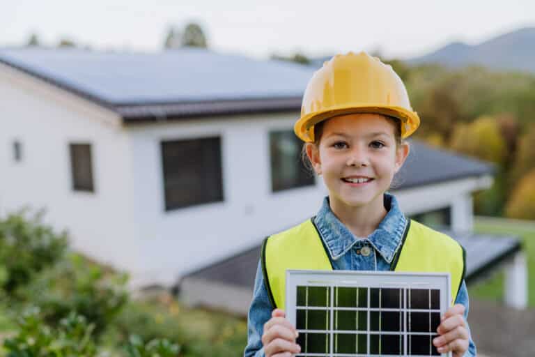 little girl with protective helmet and reflective vest holding photovoltaics solar panel. alternative energy, saving resources and sustainable lifestyle concept.